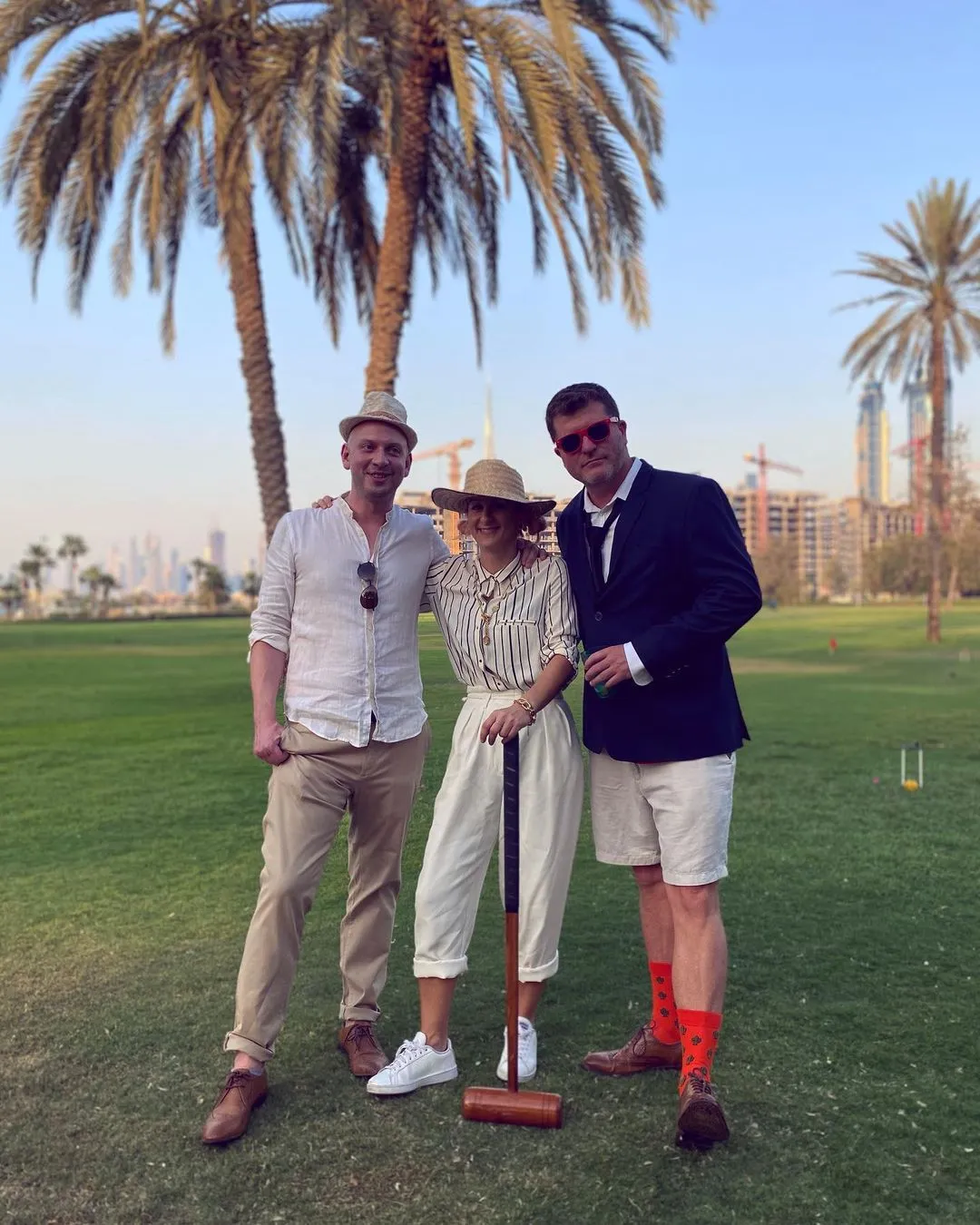 Three club members in summer whites with mallets on the lawn, palm trees behind